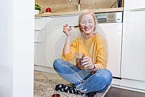 Beautiful young albino girl in casual clothes tasting delicious chocolate spread while sitting on the wooden floor in the domestic