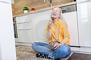 Beautiful young albino girl in casual clothes tasting delicious chocolate spread while sitting on the wooden floor in the domestic
