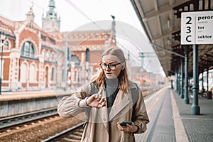 Beautiful young angry scared girl looking at her watch at the train station, holiday travel concept.