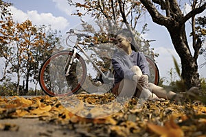 Beautiful young asia woman sitting next to her bike outdoors at full of beautiful orange flower background