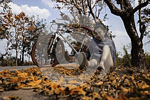 Beautiful young asia woman sitting next to her bike outdoors at palash tree with full of beautiful orange flower background