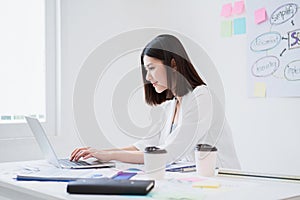 Beautiful young asian business woman looks happy and concentrate working with her laptop while sitting in the white office in good