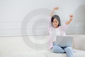 Beautiful young asian businesswoman sitting on sofa and working from home and break while stretch arm for relax.