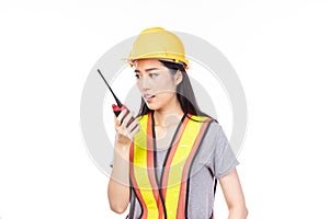 Beautiful young asian construction female worker in yellow helmet and reflective vest and using walkie talkie for talking with