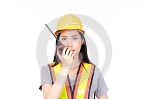 Beautiful young asian construction female worker in yellow helmet and reflective vest and using walkie talkie for talking with