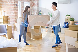 Beautiful young asian couple looking happy, holding a big cardboard box smiling excited moving to a new home