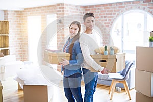 Beautiful young asian couple looking happy holding cardboard boxes, smiling excited moving to a new home