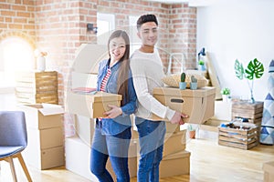 Beautiful young asian couple looking happy holding cardboard boxes, smiling excited moving to a new home