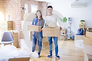 Beautiful young asian couple looking happy holding cardboard boxes, smiling excited moving to a new home