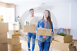 Beautiful young asian couple looking happy holding cardboard boxes, smiling excited moving to a new home