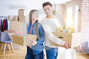 Beautiful young asian couple looking happy holding cardboard boxes, smiling excited moving to a new home