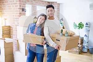 Beautiful young asian couple looking happy holding cardboard boxes, smiling excited moving to a new home