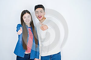 Beautiful young asian couple over white isolated background doing happy thumbs up gesture with hand