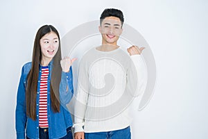 Beautiful young asian couple over white isolated background smiling with happy face looking and pointing to the side with thumb up