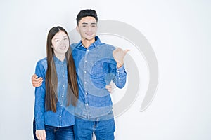 Beautiful young asian couple over white isolated background smiling with happy face looking and pointing to the side with thumb up