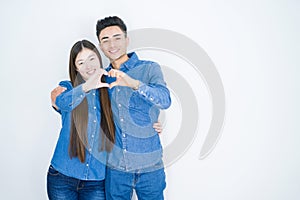 Beautiful young asian couple over white isolated background smiling in love doing heart symbol shape with hands