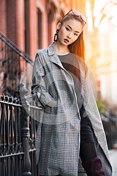 Beautiful young Asian fashion model woman walking on city street wearing jacket and sunglasses.