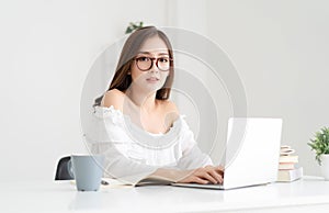 Beautiful young Asian female student using laptop and looking at camera while sitting in living room at home. Education,