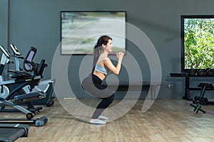 Beautiful young asian girl is wearing workout clothes and doing squat exercises at the fitness center