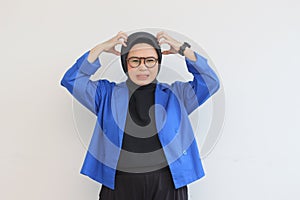 beautiful young asian muslim woman, wearing glasses and blue blazer is angry holding her head