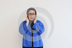 beautiful young Asian Muslim woman, wearing glasses and blue blazer with awe gestures while smiling