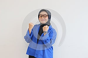 beautiful young Asian Muslim woman, wearing glasses and blue blazer with fists clenched in spirit gesture