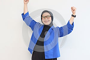 beautiful young Asian Muslim woman, wearing glasses and blue blazer with happy expression while clenching fist