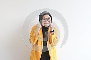 beautiful young Asian Muslim woman, wearing glasses and yellow blazer with happy expression while clenching fist