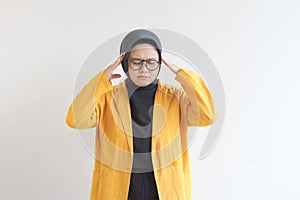 Beautiful young Asian Muslim woman, wearing glasses and yellow blazer is scratching head with confused expression