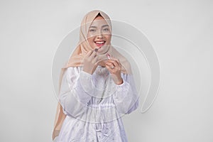 Beautiful young Asian Muslim woman wearing white dress and hijab putting on makeup applying lipstick. Fashion and cosmetics beauty