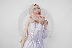 Beautiful young Asian Muslim woman wearing white dress and hijab putting on makeup applying lipstick. Fashion and cosmetics beauty