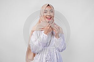 Beautiful young Asian Muslim woman wearing white dress and hijab putting on makeup applying lipstick. Fashion and cosmetics beauty