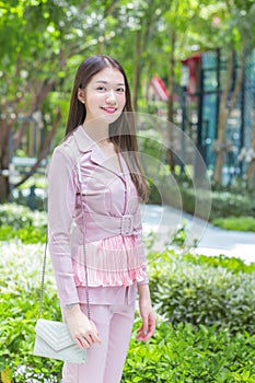 Beautiful young Asian professional business woman with long hair wearing pink shirt is smiling outdoor in the garden front of the
