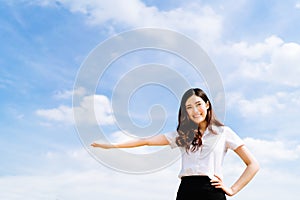 Beautiful young asian university or college student woman doing advertising or product presenting pose, copy space on blue sky