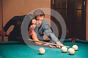 Beautiful young asian woman aiming into white billiard ball. Her boyfriend stand besides. He help her to play. They are in