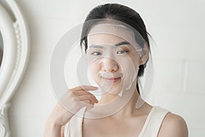 Beautiful young asian woman applying sheet facial mask and looking mirror at home, Girl applying cosmetic and makeup with skincare