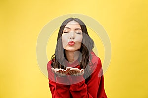 Beautiful young Asian woman blow a kiss on yellow background.