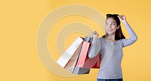 Beautiful young Asian woman carrying shopping bags looking surprised and happy isolated on yellow banner background with copy spac