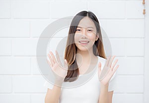 Beautiful young asian woman confident gesture say hello or greeting with waving her hand on cement background.