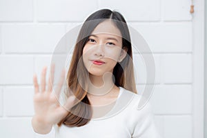 Beautiful young asian woman confident gesture say hello or greeting with waving her hand on cement background.