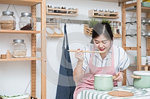 Beautiful young asian woman cooking and testing soup food in the kitchen, female cook food by herself in quarantine period,Social