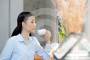 Beautiful young asian woman drinking coffee and smile in the morning at cafe, girl sitting in coffee shop