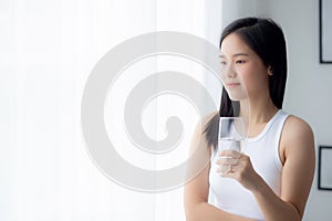 Beautiful young asian woman drinking glass of water mineral pure with fresh and happy at home.