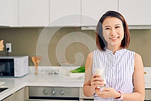 Beautiful young Asian woman drinking milk in the kitchen at home