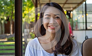 A beautiful young Asian woman feels happy, smiling and looking relaxed at the camera in a coffee shop. Smiling Asian girl