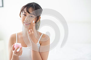 Beautiful young asian woman happy applying cream or lotion with moisturizer to skin face