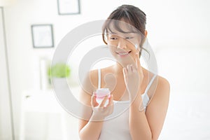 Beautiful young asian woman happy applying cream or lotion with moisturizer to skin face
