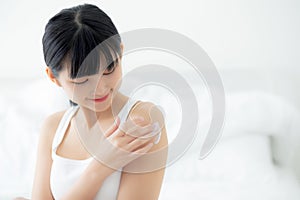 Beautiful young asian woman happy applying cream or lotion with moisturizer to skin on shoulder.