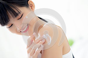Beautiful young asian woman happy applying cream or lotion with moisturizer to skin on shoulder.
