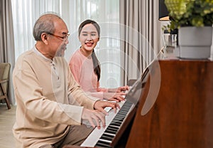 Beautiful young Asian woman and her father sitting playing piano together happy in the living room at home